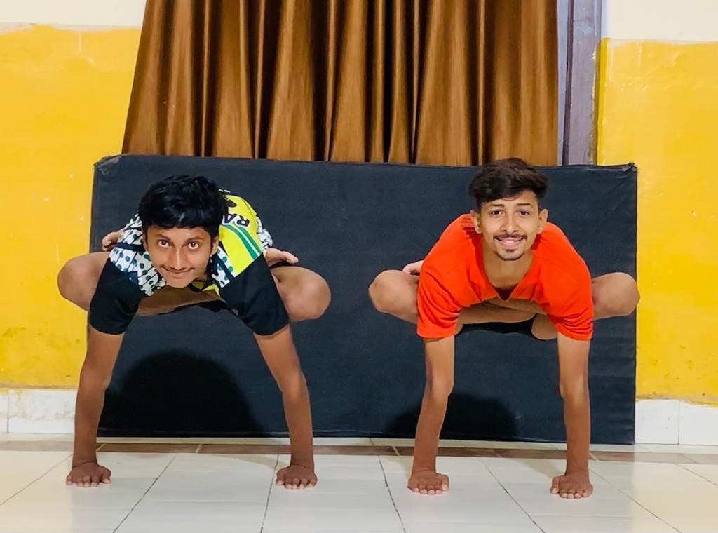 Two practitioners in an arm-balance pose indoors